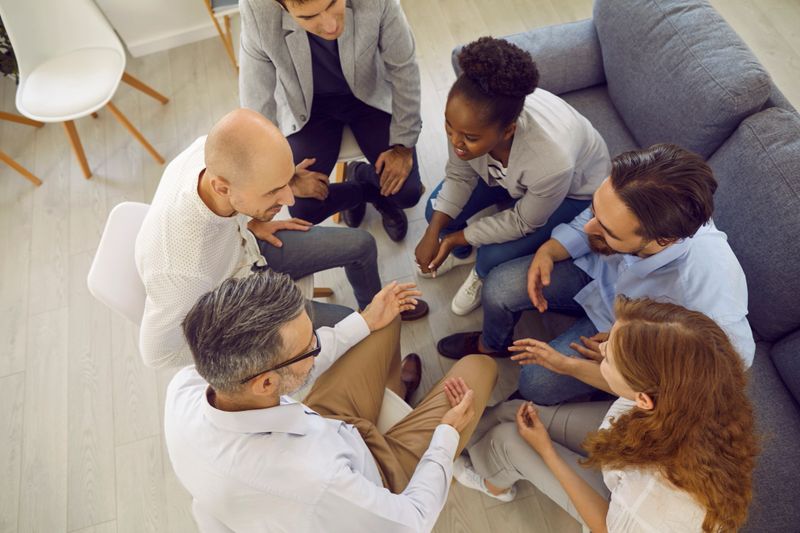 Diverse multiracial people sit in circle talking together in psychological group on therapy session, top view. Group psychotherapy, therapy, psychological help, mental health and support concept.