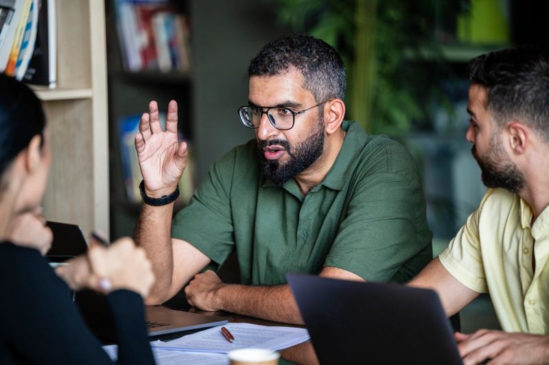 Serious Middle Eastern businessman talking to co-workers with hand raised, decision making, problem solving, strategy