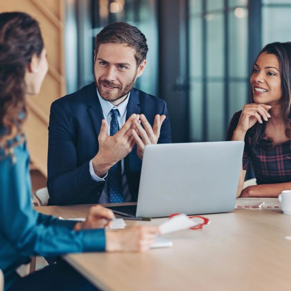Three professionals engaged in a business meeting around a laptop.