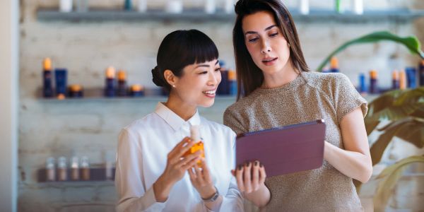 Two women discussing a product while looking at a tablet in a skincare store.