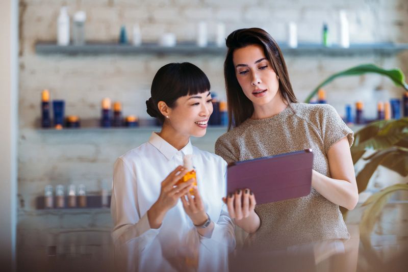 Two women discussing and using a digital tablet, set in a contemporary workspace environment.