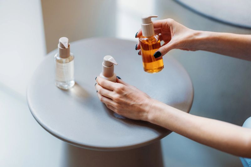 A close-up of hands arranging bottles containing skincare products on a clean and minimalist surface.