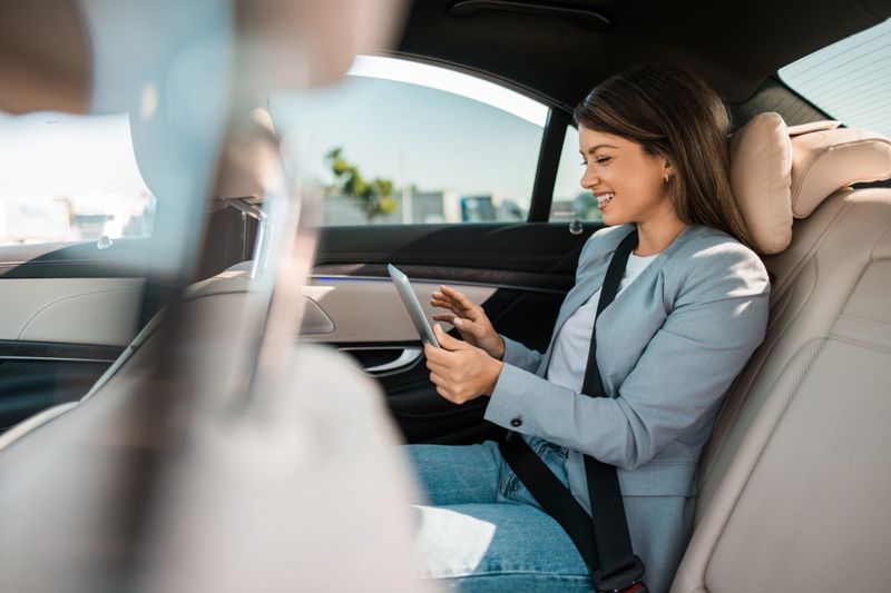 Cheerful businesswoman sitting on a backseat of luxurious automobile and using digital tablet.