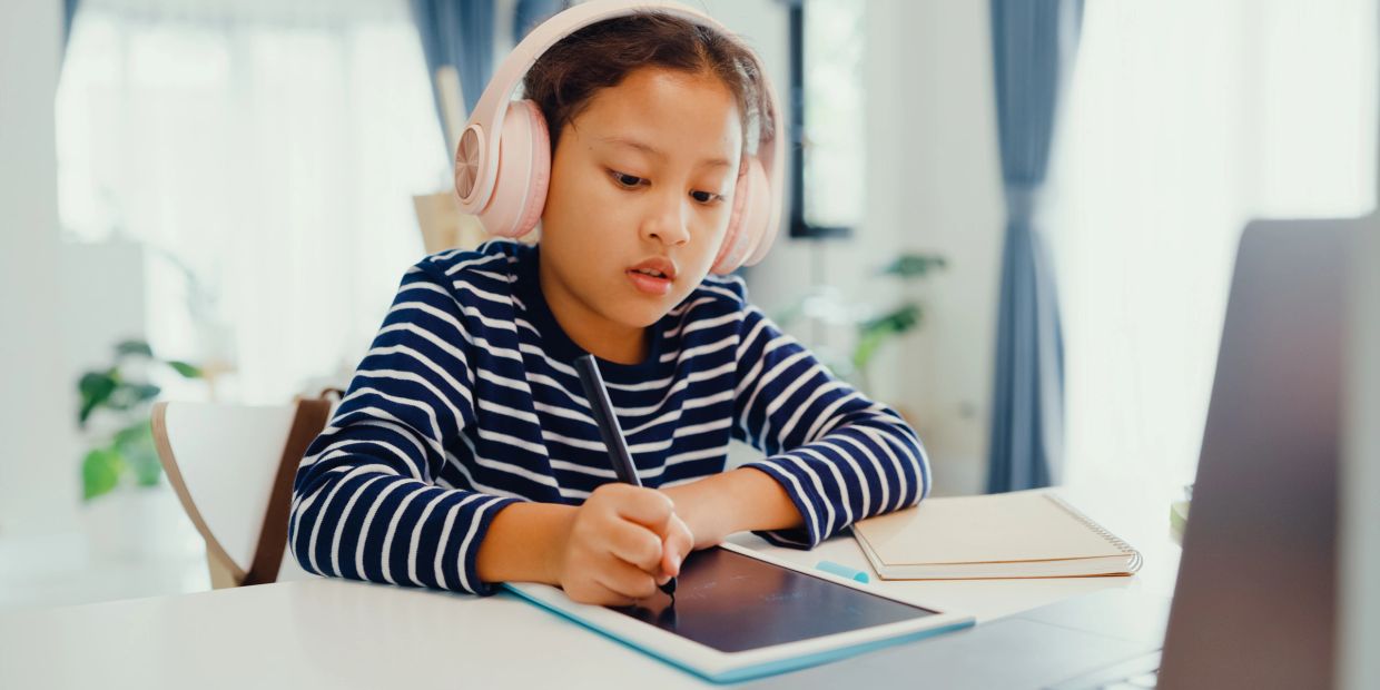 Girl wearing headphones using a digital tablet to draw.