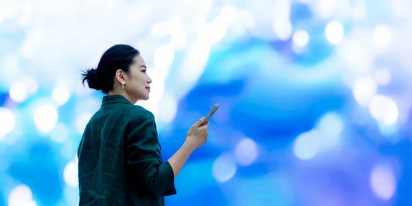Woman in green jacket holding phone against a blue bokeh background.