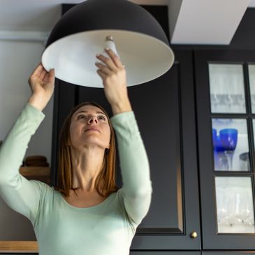 Woman changing a light bulb in a modern kitchen.