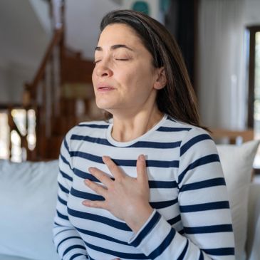 A woman practices deep breathing with eyes closed indoors.