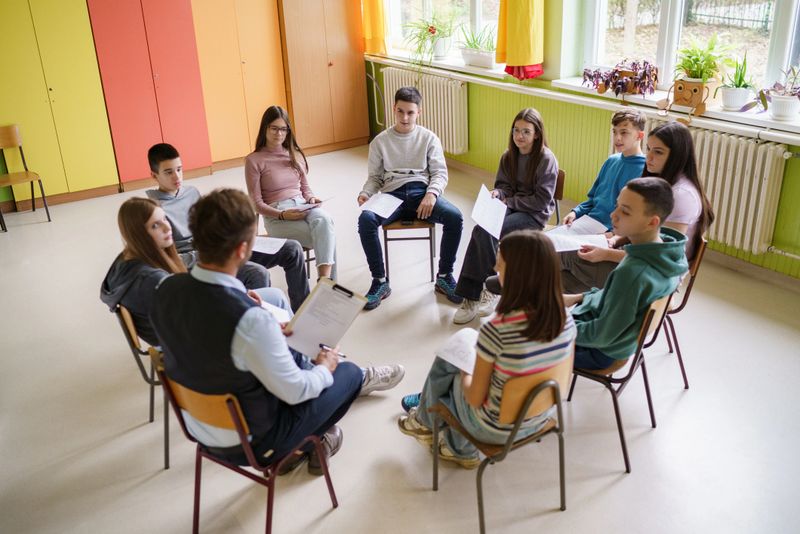A group of teenagers sit on chairs in a circle with the teacher and go through the material
