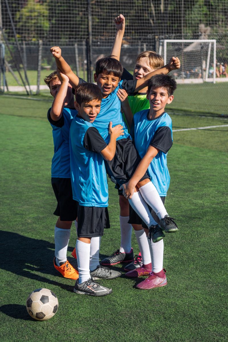 A joyful group of young boys celebrating after a soccer game played on an outdoor field. Their blue uniforms and vivid expressions reflect their team spirit, excitement, and camaraderie.