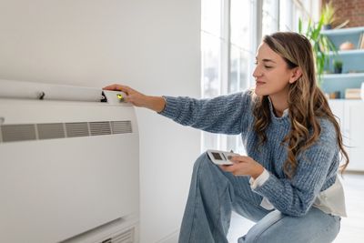 Woman adjusting thermostat on heater.