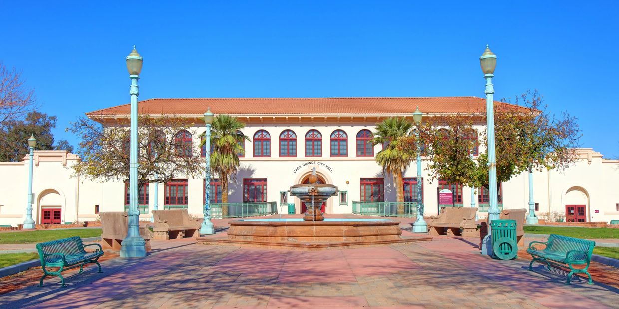 Casa Grande City Hall with fountain, benches, and palm trees under a clear blue sky.