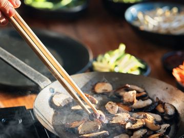 Cooking sliced mushrooms in a pan with chopsticks.