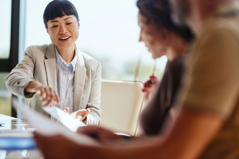 Happy Asian real estate agent going through plans with her customers during a meeting in the office.