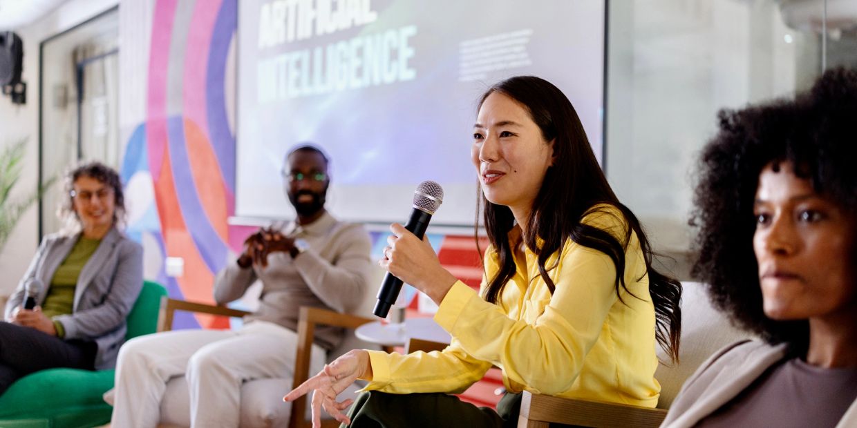 Woman speaks with microphone at AI panel discussion.