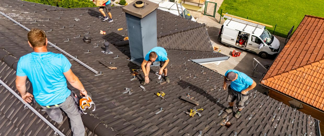 Workers in blue shirts installing solar panels on a rooftop on a sunny day.