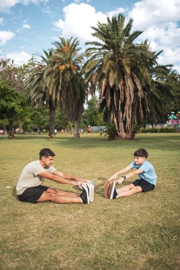 Man and boy stretching together on grass in a park.