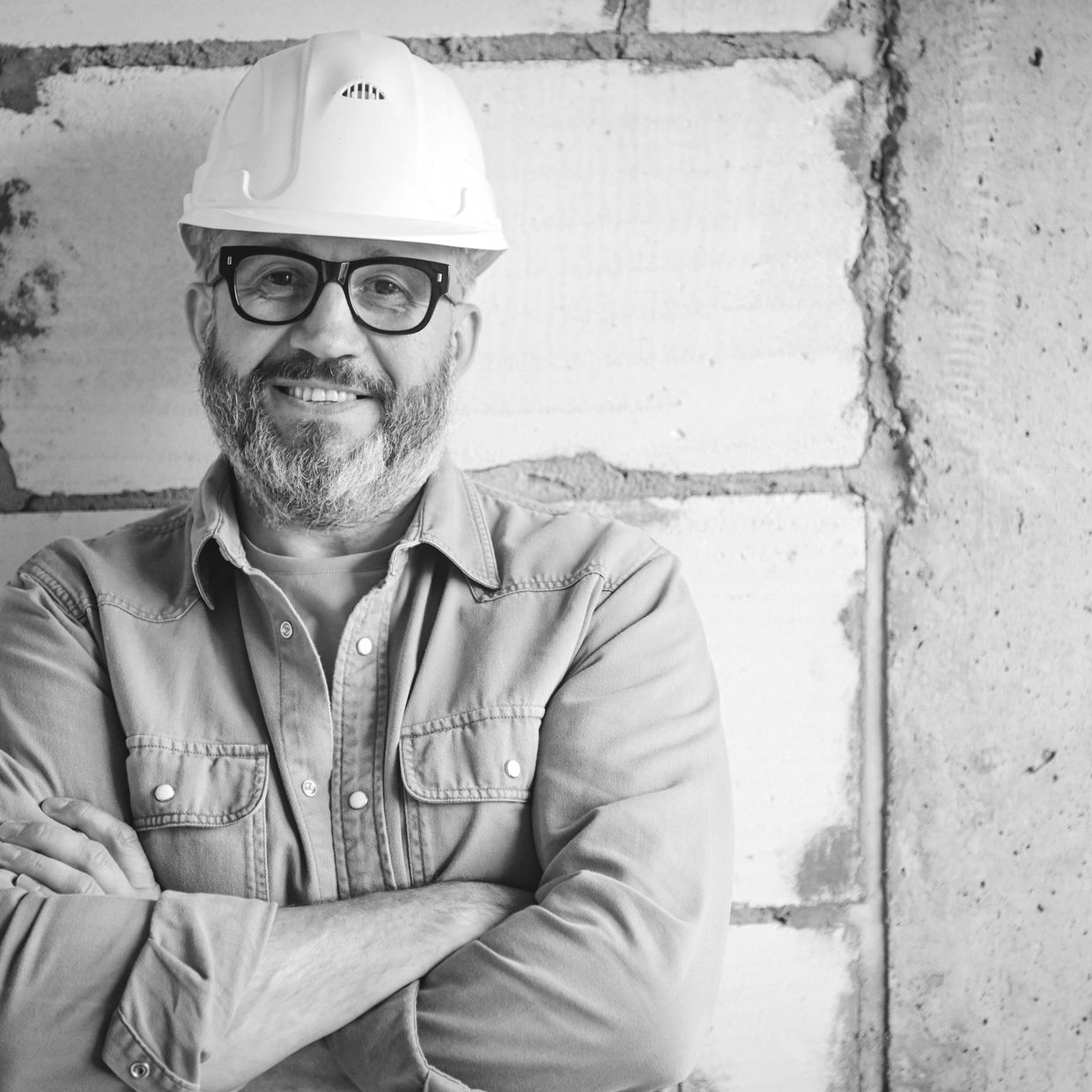 Smiling construction worker wearing a white helmet and glasses, standing with arms crossed.