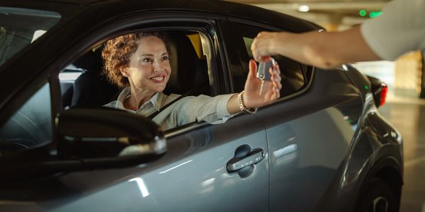 A woman happily receives car keys while sitting in a parked car.
