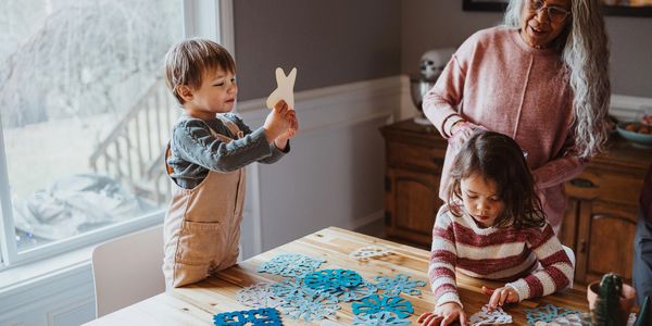 Children making paper snowflakes with an older woman supervising.