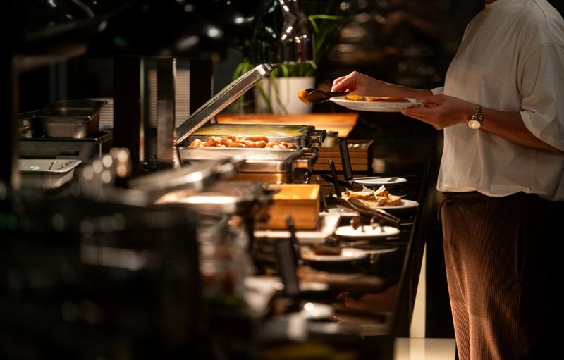 Unrecognizable man serving himself at buffet breakfast, dark, copy space