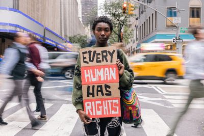 People hold signs promoting pride and action in a lively crowd.