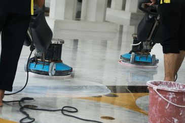 
The image shows two individuals operating floor polishing machines on what appears to be a marble