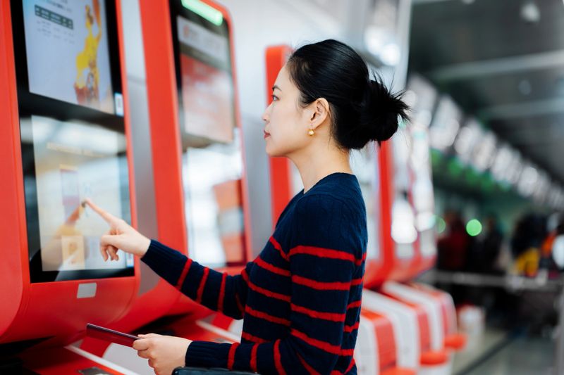 Asian businesswoman using self check-in machine at the airport terminal getting the boarding pass, Technology in airport.Passenger scanning ticket on smart phone at airport.