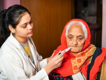Young female doctor checking temperature of an elderly woman.