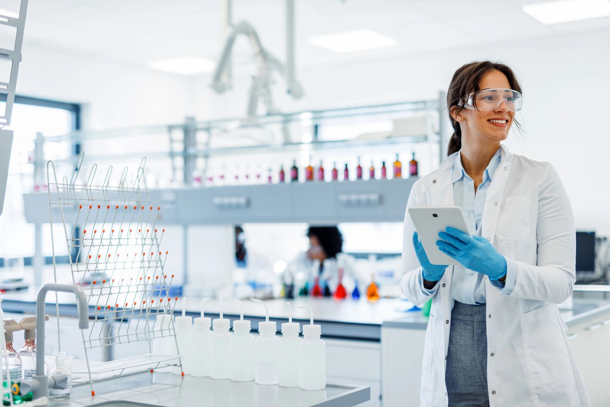 Female scientist in a modern lab holding a tablet and smiling.