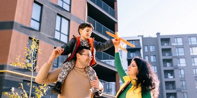 A joyful family plays with a toy airplane outside urban apartments.