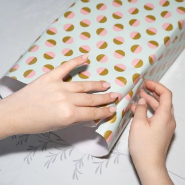 Hands wrapping a gift with patterned paper.