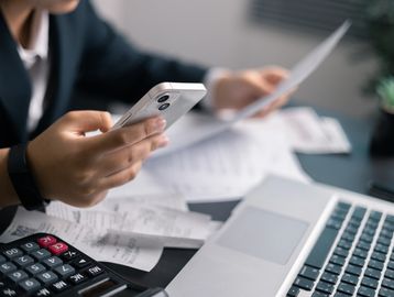 Person managing finances with phone, receipts, calculator, and laptop.