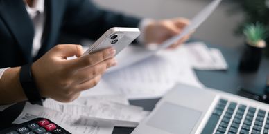 Person managing finances with phone, receipts, calculator, and laptop.