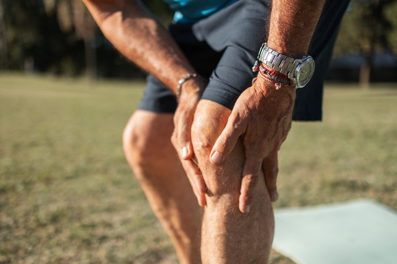 A close-up view of a senior man holding his knee, indicating joint discomfort, captured during an outdoor exercise session. This image portrays health challenges associated with aging and the importance of wellness.