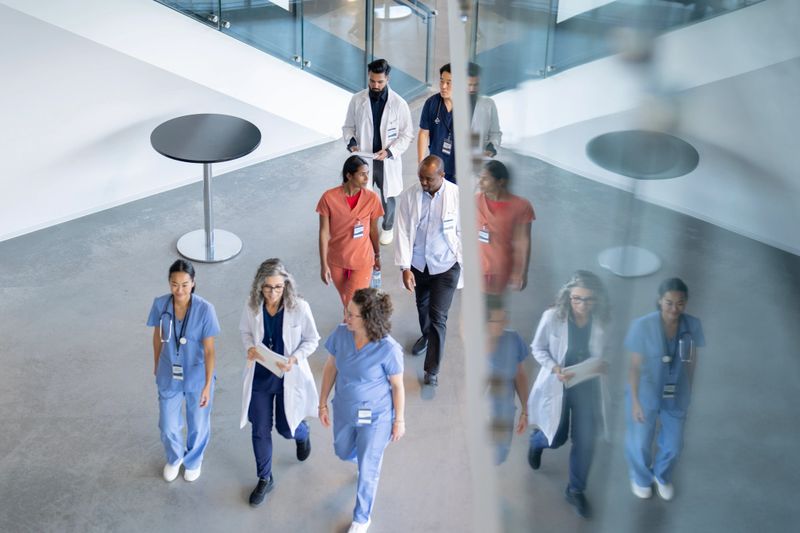 A large group of medical professionals are seen walking in a hall as they make their way to a medical conference.  They are each dressed professionally and are seen from above in this aerial view.