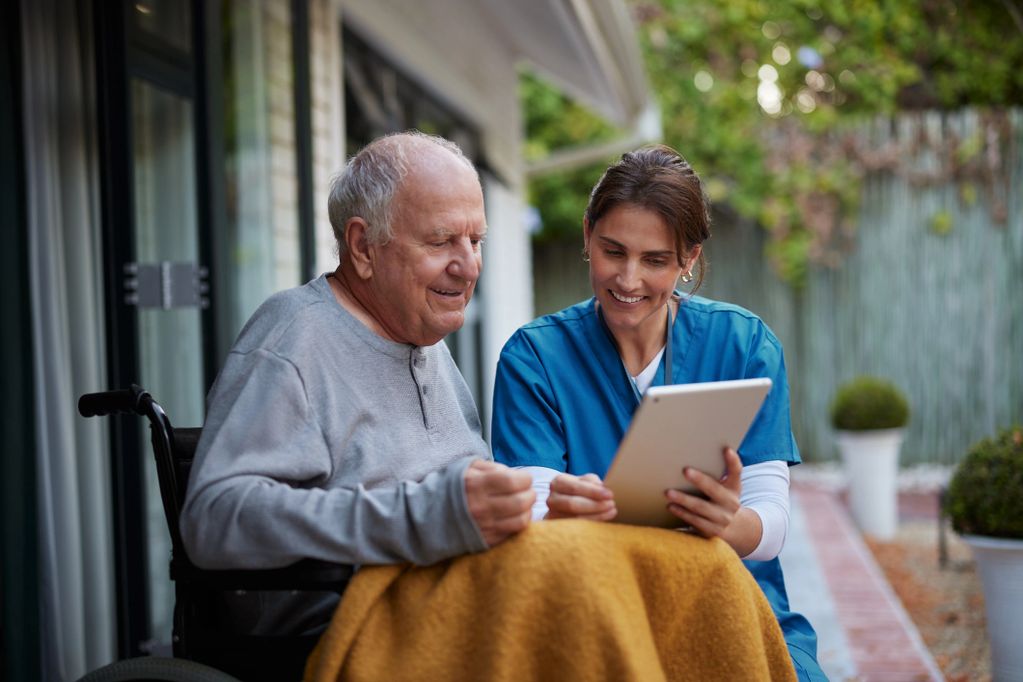 A nurse and an elderly man looking at something on a tablet.
