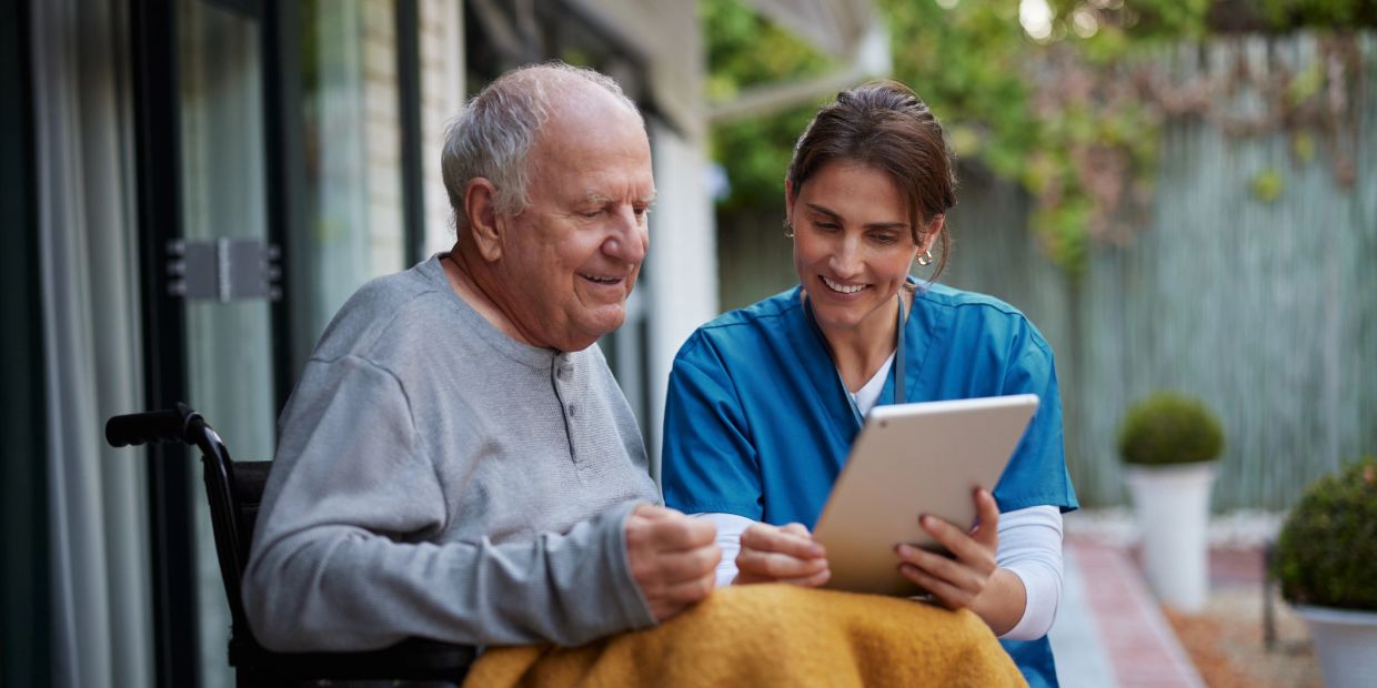 Nurse and elderly man enjoying a tablet together.