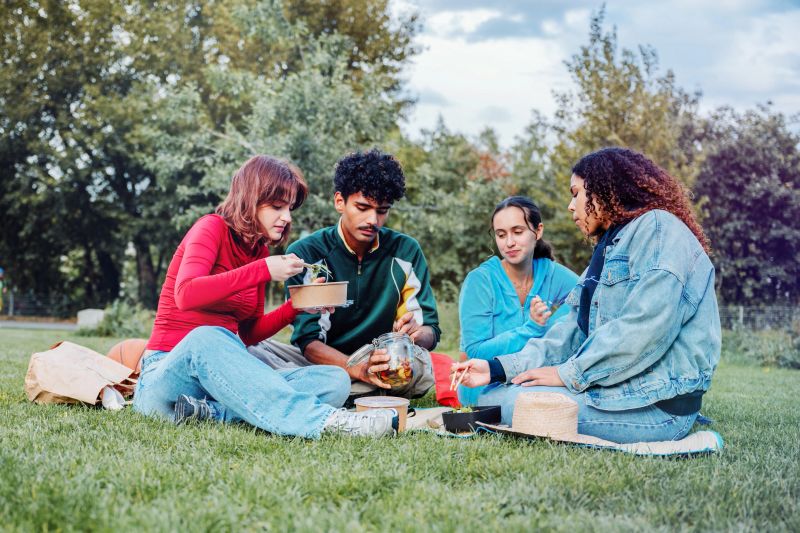four young people having picnic in the park with home prepared sustainable food