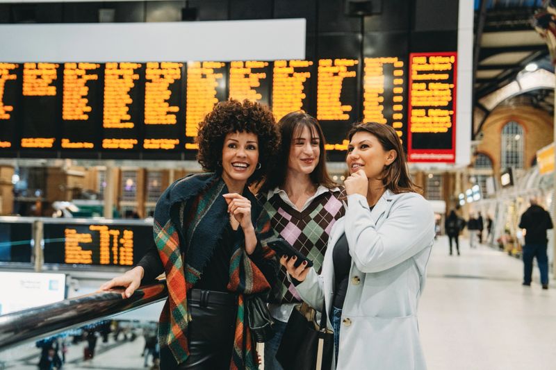 Three friends looking at the departure board at a train station in london, uk, planning their journey