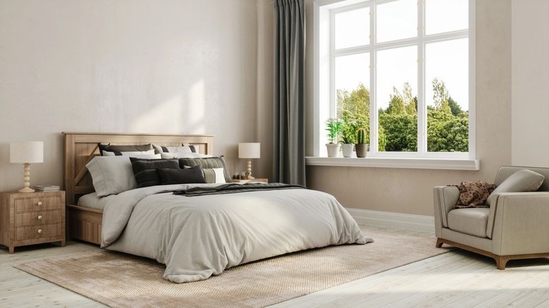 A serene bedroom with neutral tones, a large bed, wooden furniture, and a window showcasing greenery.