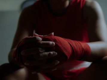 Boxer with red hand wraps sits with hands clasped.