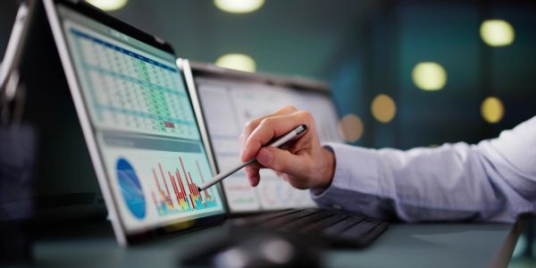 Person using a stylus on a laptop displaying charts.