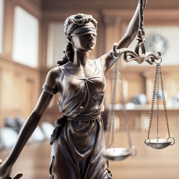 Blindfolded Lady Justice holding scales in a courtroom.