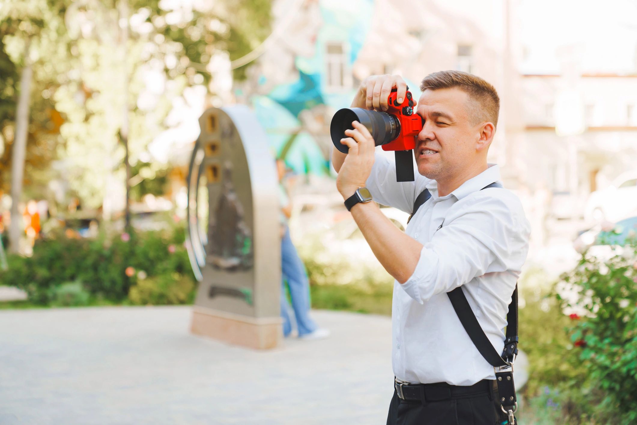 Man taking photos with a red camera outdoors in a sunny park.