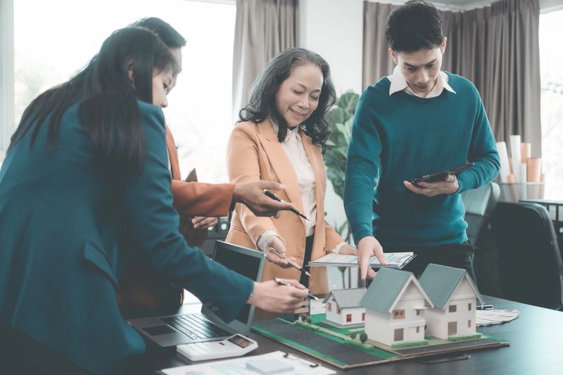 Real estate business meeting with wooden house models on documents, laptops and people discussing houses in single-family home construction Townhome, selecting materials and location for housing projects
