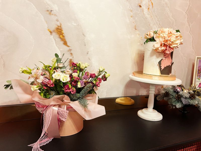 A stunning arrangement of flowers with pastel hues, accompanied by a beautifully decorated cake. Enhanced with soft lighting, this composition portrays sophistication and charm, ideal for celebrations or design inspiration.