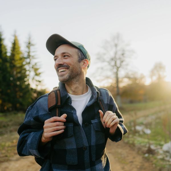 Smiling man hiking outdoors with a backpack at sunset.