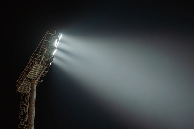 Powerful stadium lights illuminate the night sky, casting bright beams of light across the darkness, creating a dramatic and atmospheric scene