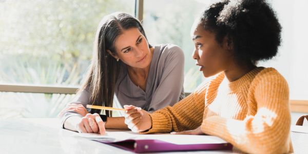 Two women discussing study material at a table.