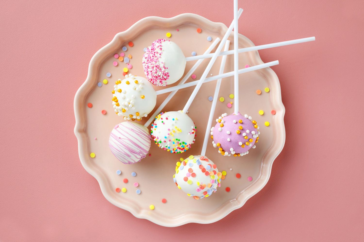 Colorful decorated cake pops on a pastel pink plate.